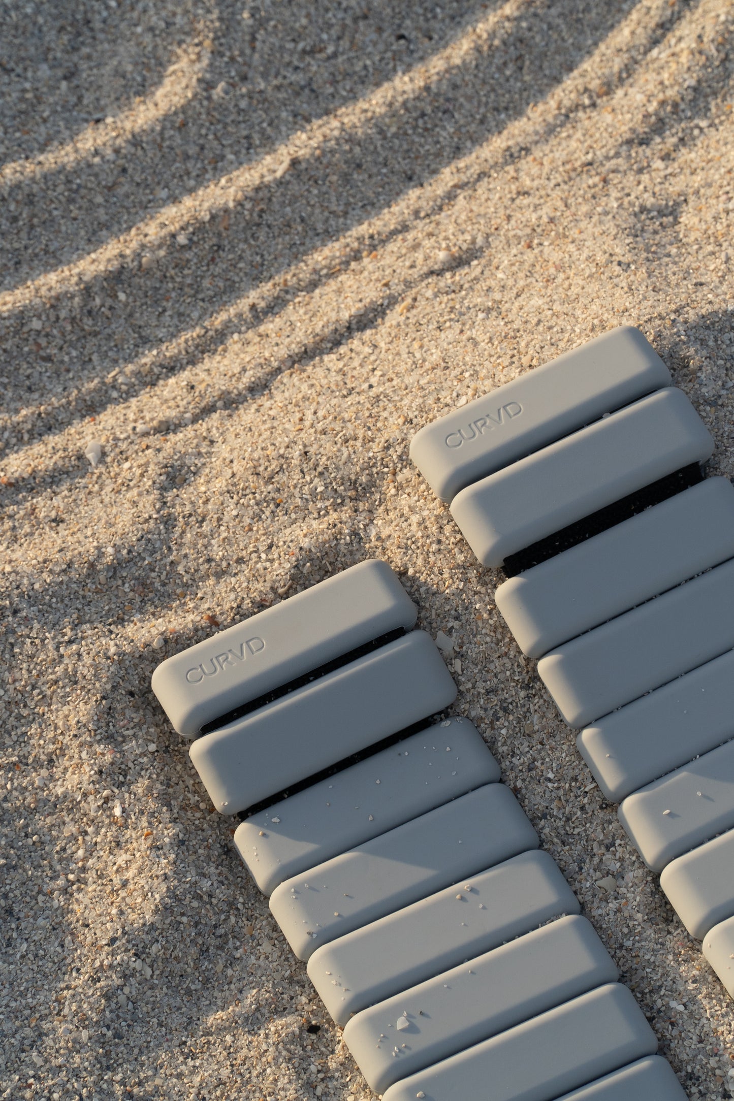 Curvd ankle weights strategically placed on the sandy beach at sunset, casting long shadows.