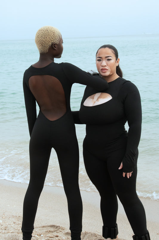 Two diverse models showcasing the sleek design and low-back feature of Curvd's Long Active Bodysuits by the seashore.