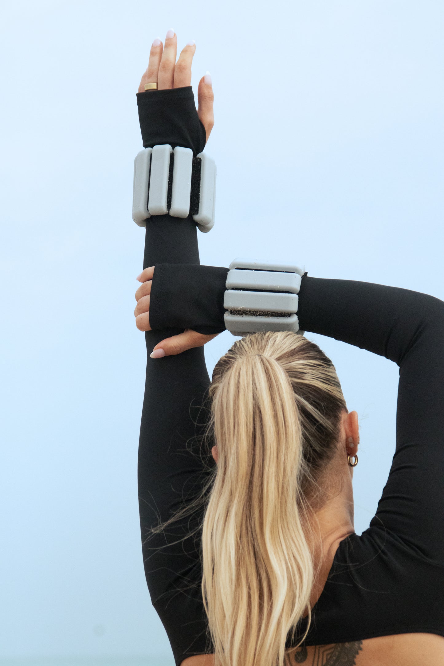 Fitness enthusiast performing a stretch with Curvd wrist weights against a serene sky backdrop.